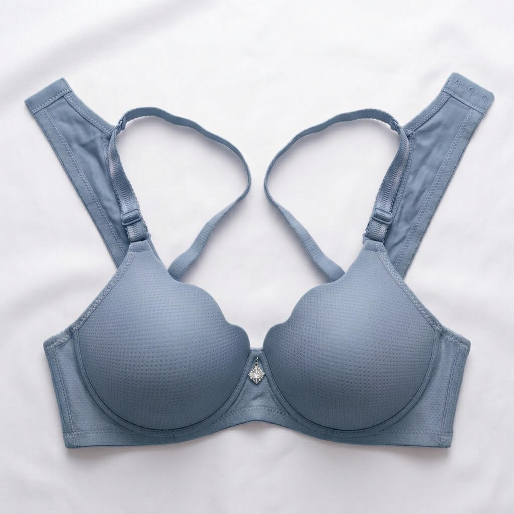 A dusty blue textured wireless bra laid flat on a white fabric background, featuring wide adjustable shoulder straps and a small rhinestone embellishment at the center front.