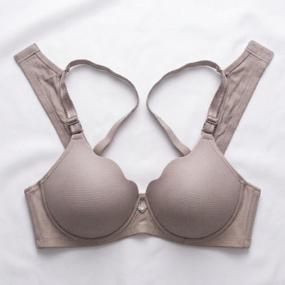 A light taupe-beige wireless underwire bra with a subtle textured dot pattern, featuring adjustable shoulder straps and a small rhinestone accent at the center gore, laid flat on a white background.