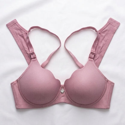 A dusty pink wireless bra with textured cups and adjustable straps, laid flat on a white fabric background.