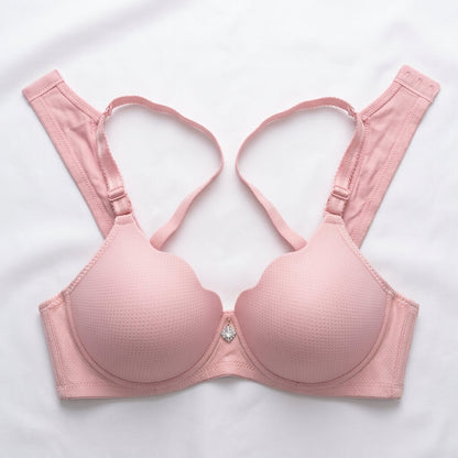 A light pink wireless underwire bra with wide adjustable shoulder straps and a small rhinestone accent at the center gore, laid flat on a white fabric background.