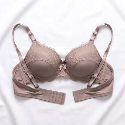 A structured wireless bra in a muted taupe-beige color, featuring textured lace cups, adjustable shoulder straps, and a central bow, laid flat on a white fabric background.
